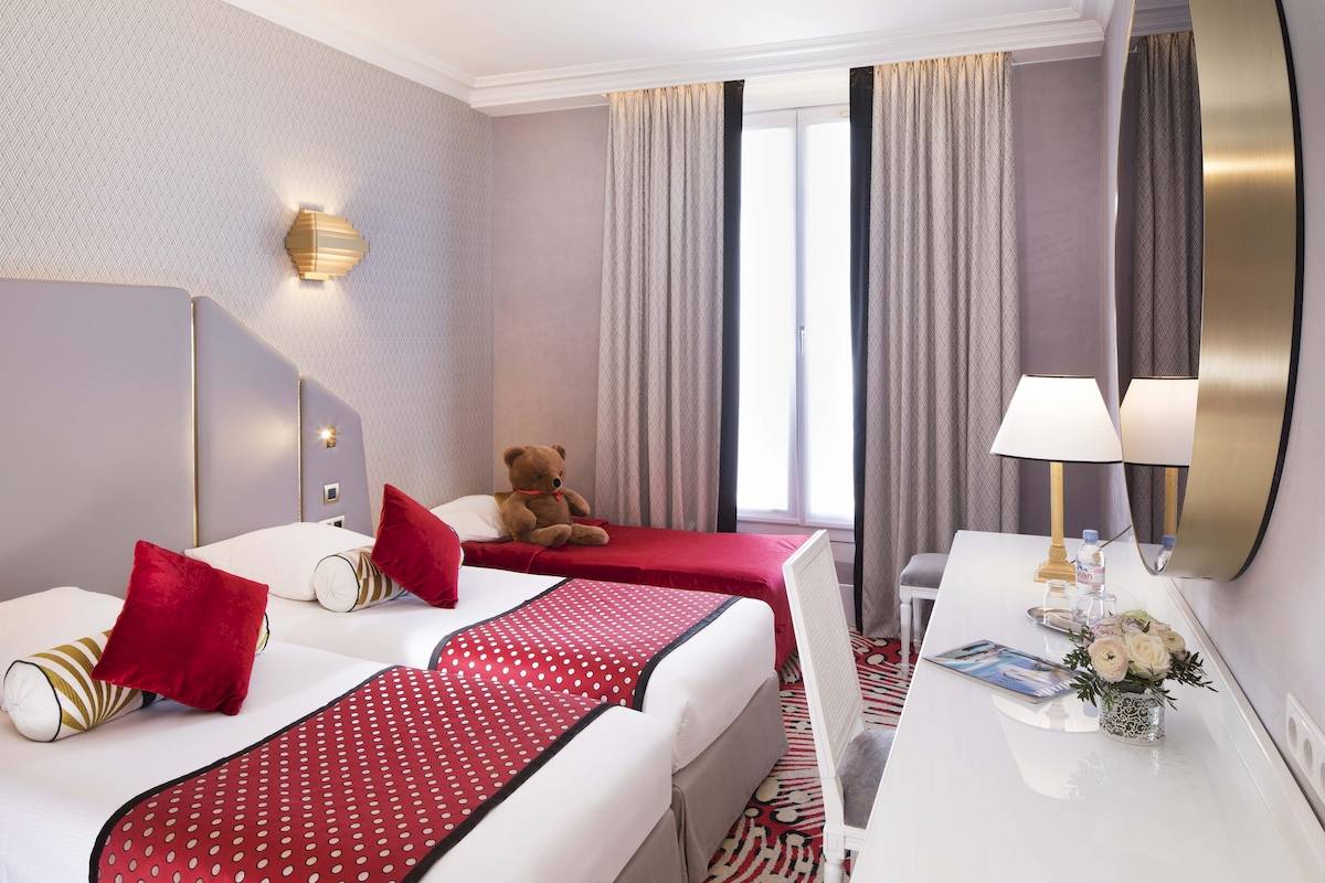 Doppelzimmer im Hotel Victor Hugo Paris Kléber mit zwei Betten, Tisch, Lampen und Teddybär