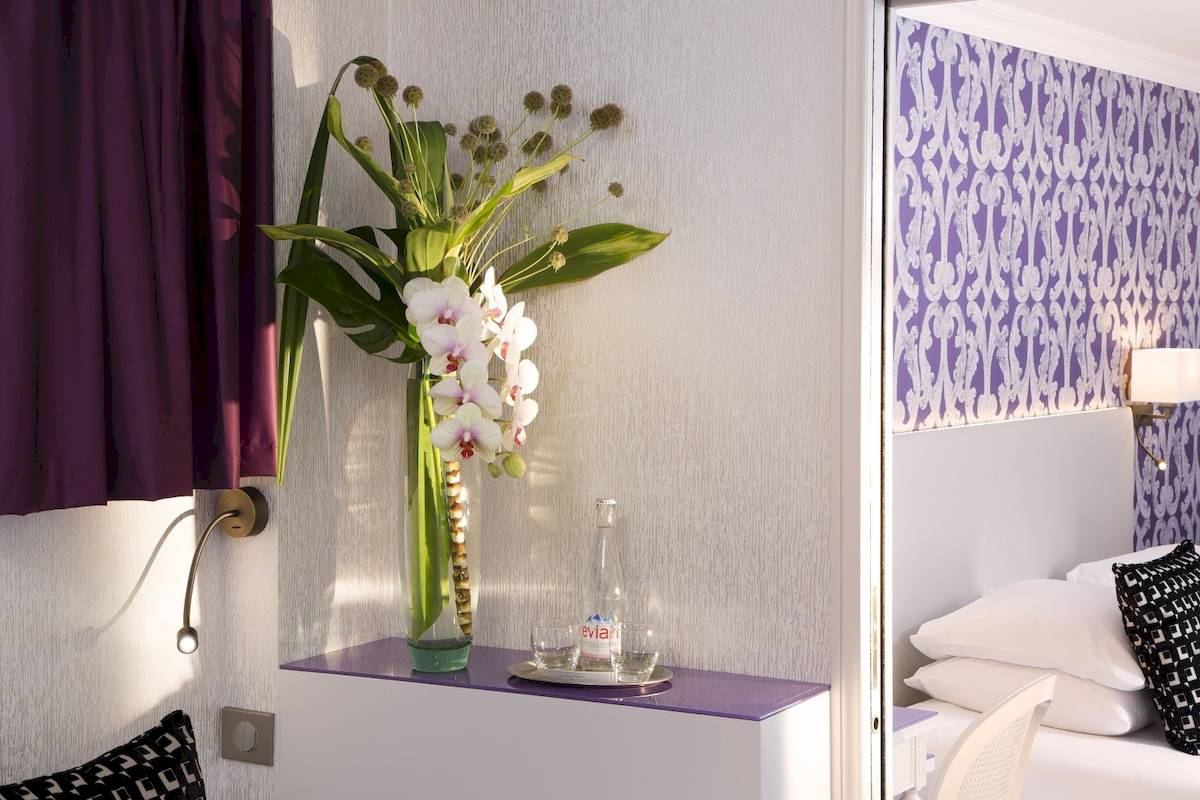 Zimmer im Victor Hugo Paris Kléber Hotel mit Blumenvase und Wasserflaschen auf einem Nachttisch.