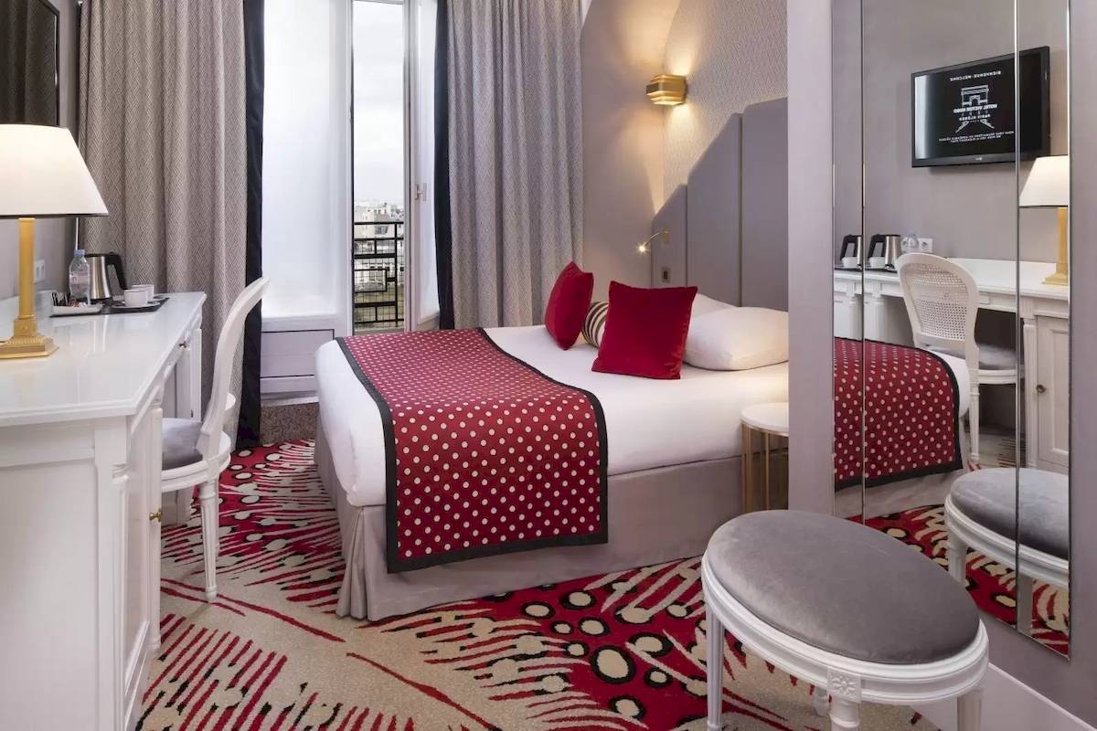 Hotelzimmer im Victor Hugo Paris Kléber mit einem Bett, roten Kissen und einem Schreibtisch.