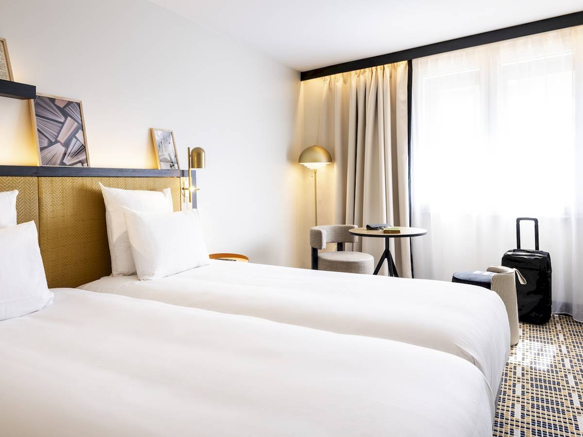 Doppelzimmer im Mercure Paris Bercy Bibliothèque mit zwei Betten, Nachttischen und einem Reisekoffer.