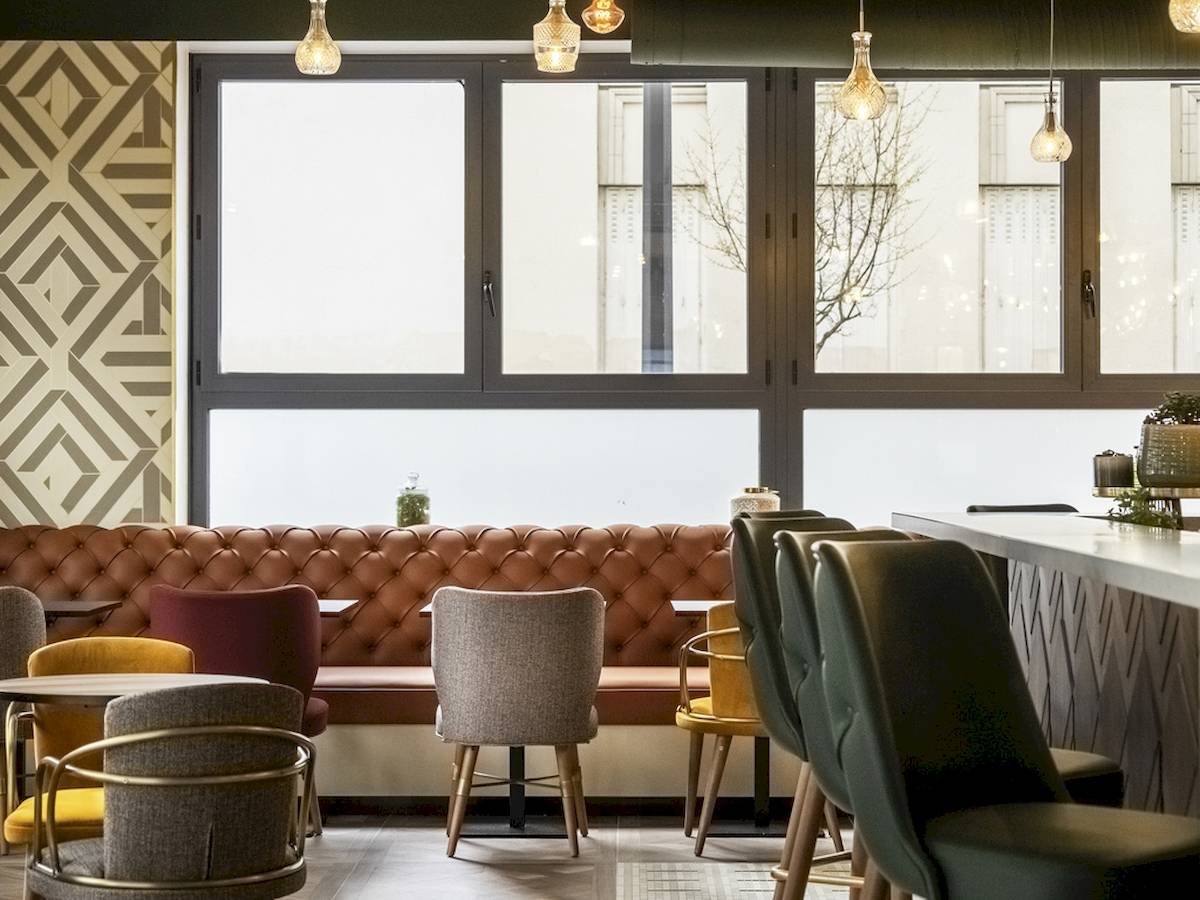 Innenansicht des Restaurants im Mercure Paris Bercy Bibliothèque Hotel mit großen Fenstern und verschiedenen Stühlen.