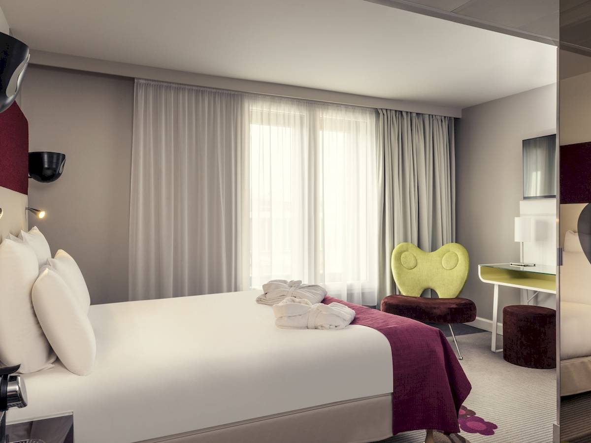 Schlafzimmer im Mercure Paris Bercy Bibliothèque Hotel mit Bett, Kissen, Bademänteln und Möbeln.
