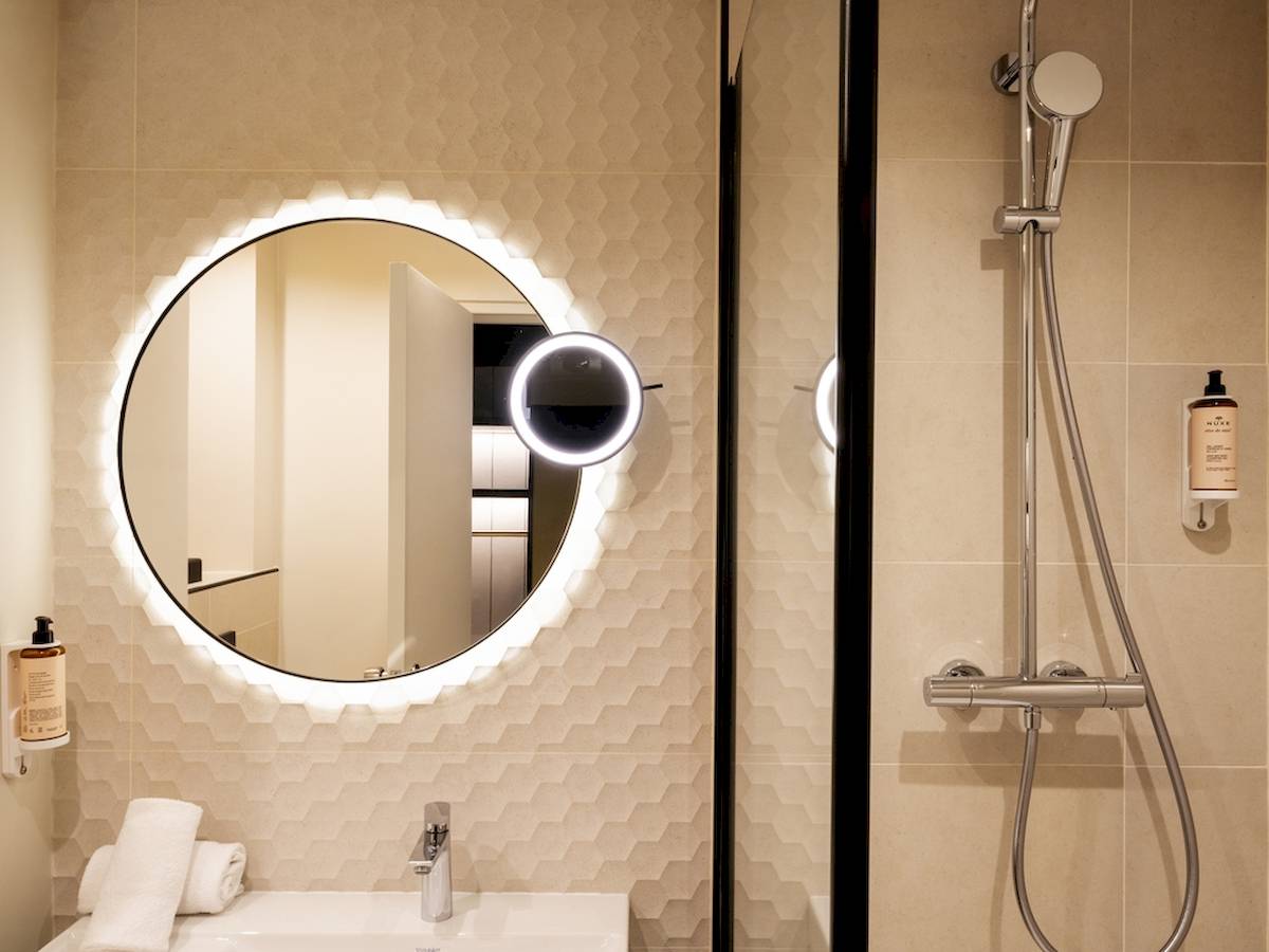 Badezimmer des Mercure Paris Bercy Bibliothèque mit beleuchtetem Spiegel und Duschvorrichtung.