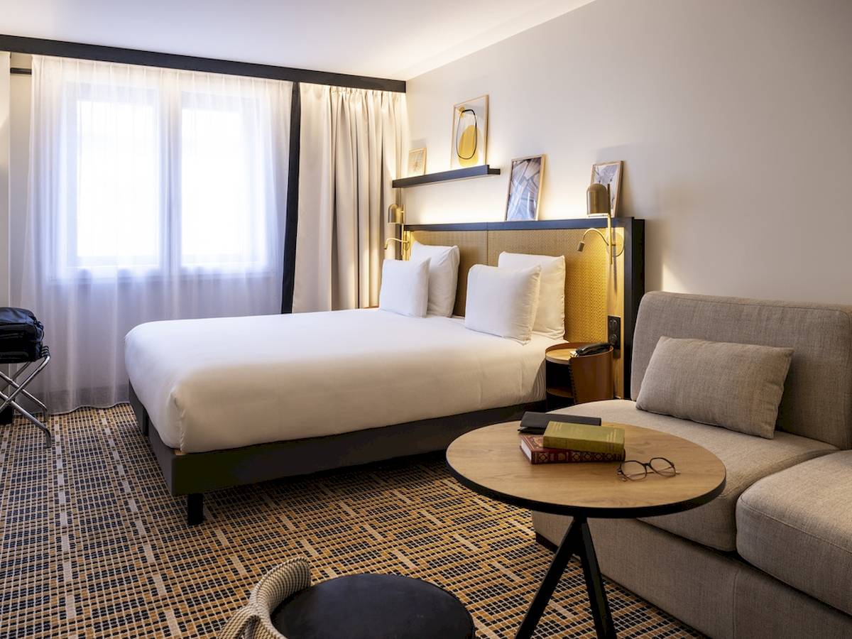 Hotelzimmer im Mercure Paris Bercy Bibliothèque mit Bett, Sofa, Tisch und Büchern.
