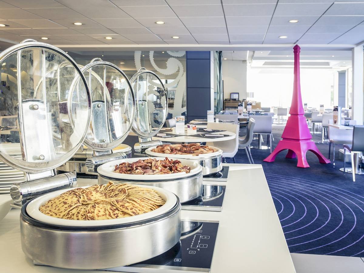 Buffet-Tisch mit verschiedenen Speisen, darunter gebratener Speck, Waffeln und eine pinke Eiffelturm-Skulptur im Hintergrund.