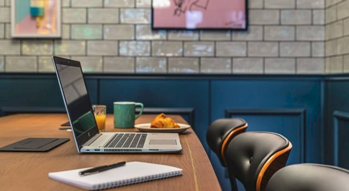 Laptop auf Konferenztisch im ReMIX Hotel mit Kaffee, Croissant und Notizbuch