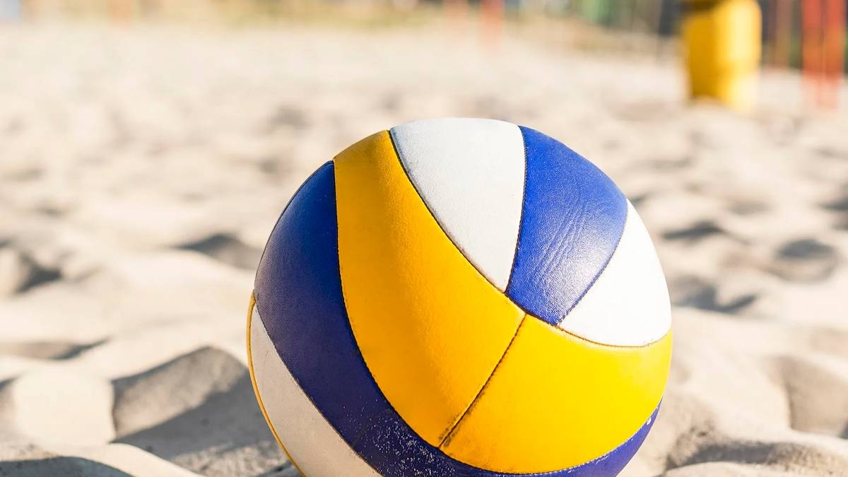 Ein Volleyball liegt auf einem Sandstrand, mit gelben, blauen und weißen Farben.