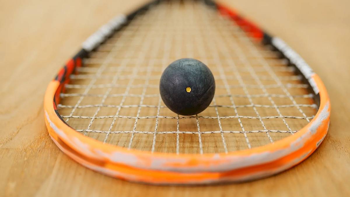Ein orangefarbener Tennisschläger mit einem schwarzen Ball auf einem Holzboden.