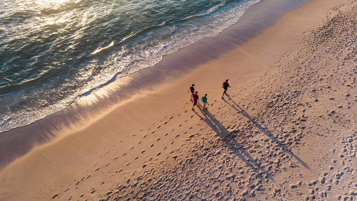 Familie am Strand während des Sonnenuntergangs, mehrere Personen gehen in Richtung Wasser.