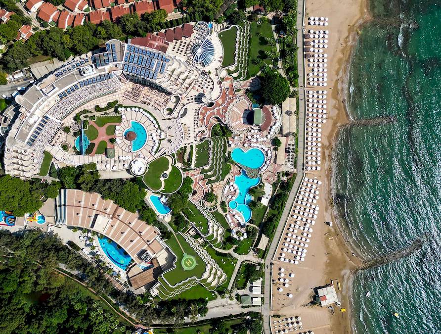 Luftaufnahme des Sonnenaufgang Queen Luxury Hotels mit mehreren Swimmingpools und Sonnenliegen am Strand