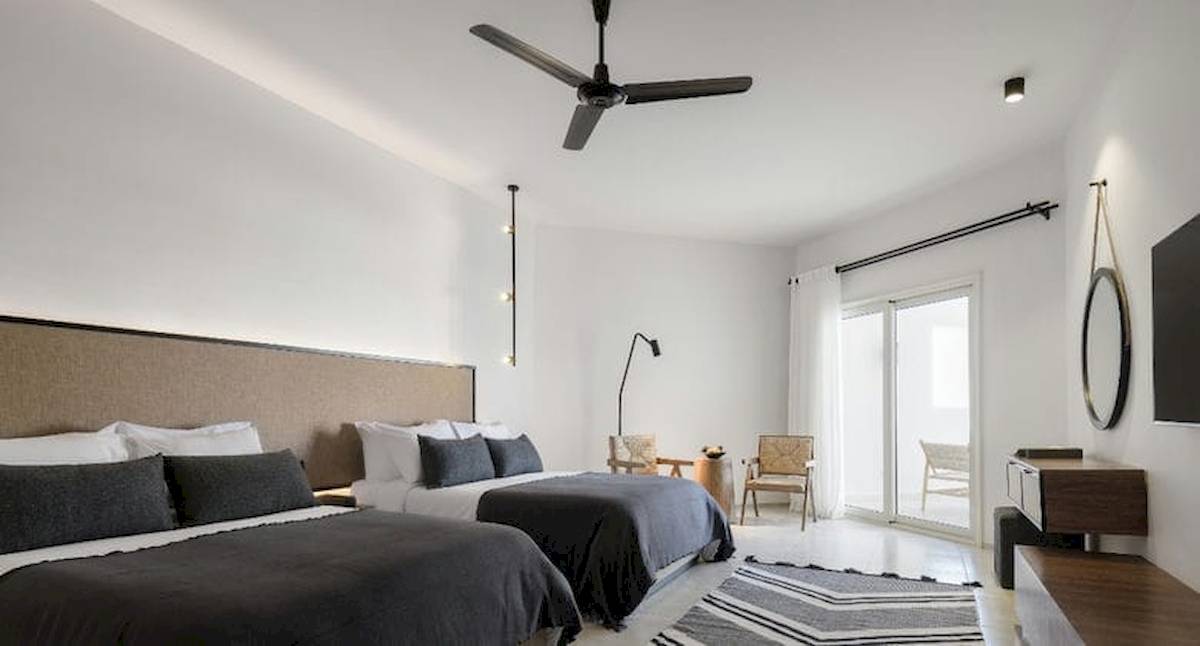 Doppelbettzimmer im Serry Beach Resort mit weißen Wänden, einer großen Glastür und einem Ventilator an der Decke.