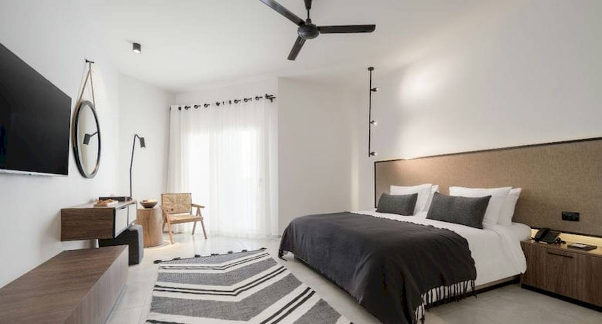 Ein modernes Hotelzimmer im Serry Beach Resort mit weißem Interieur, einem Bett, einem Fernseher und einer Deckenventilator.