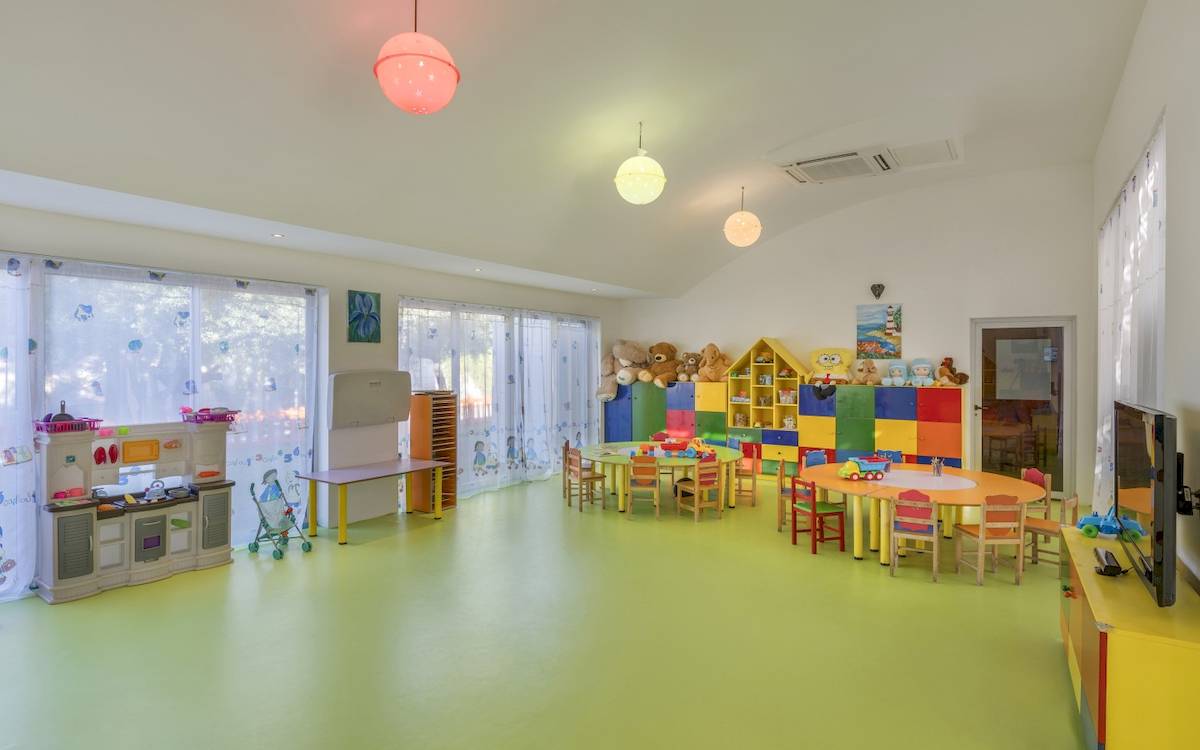 Kinderzimmer im Dobedan Exclusive Hotel & Spa Belek mit gelbem Boden, bunten Möbeln und Spielzeug.