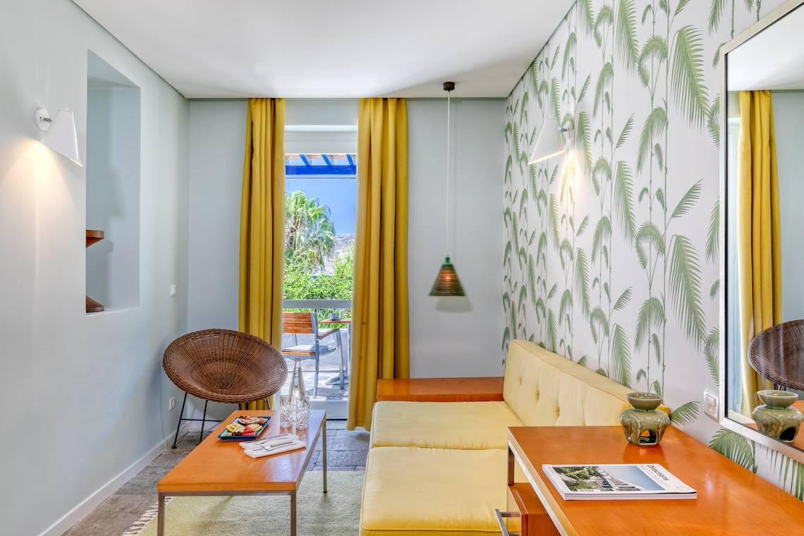 Wohnzimmer im Mykonos Theoxenia Boutique Hotel mit gelber Couch und blauem Tisch.