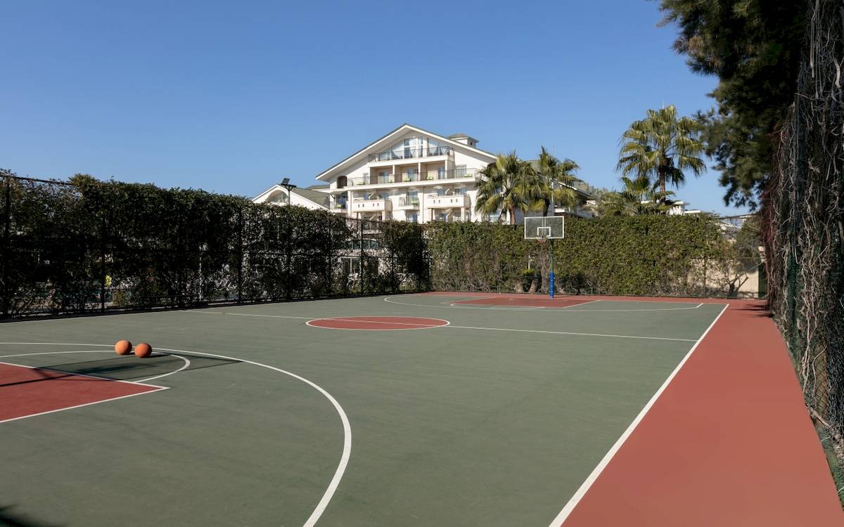 Basketballplatz vor dem Dobedan Exclusive Hotel & Spa Belek mit leerem Spielfeld und einer Villa im Hintergrund.