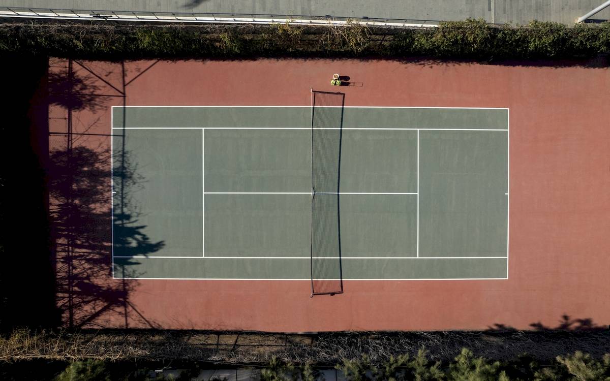 Ein Tennisplatz aus der Vogelperspektive mit roten Seitenwänden und einem Netz in der Mitte.