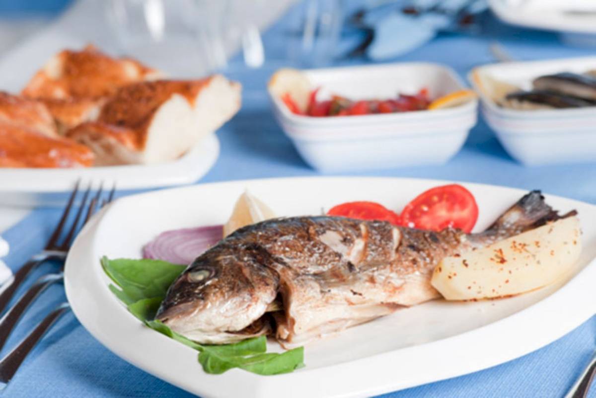 Ein gebratener Fisch auf einem weißen Teller mit Kartoffeln und Gemüse