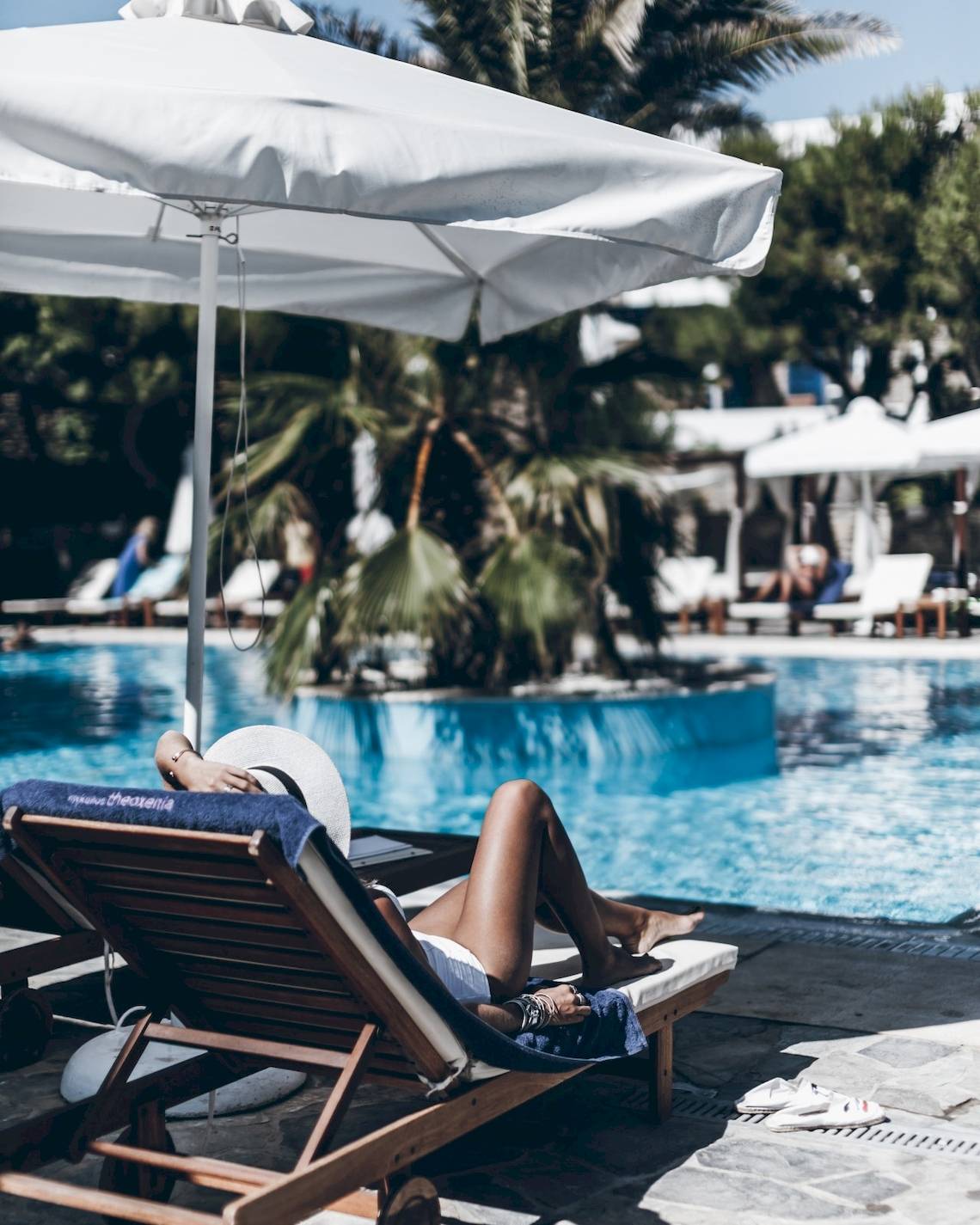 Gäste entspannen am Pool im Mykonos Theoxenia Boutique Hotel unter einem Sonnenschirm.