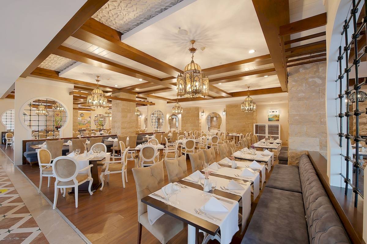 Innenansicht des Restaurants im Sentido Kamelya Fulya Hotel mit Tisch und Stühlen, Holzboden und Steinwänden.