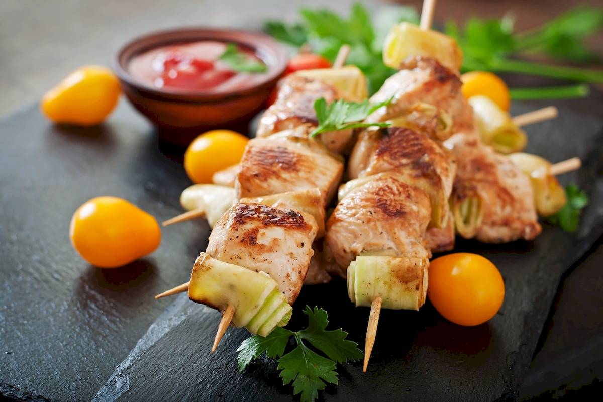 Gegrillte Hähnchenspieße mit Zucchini und Sauce auf einem schwarzen Teller.