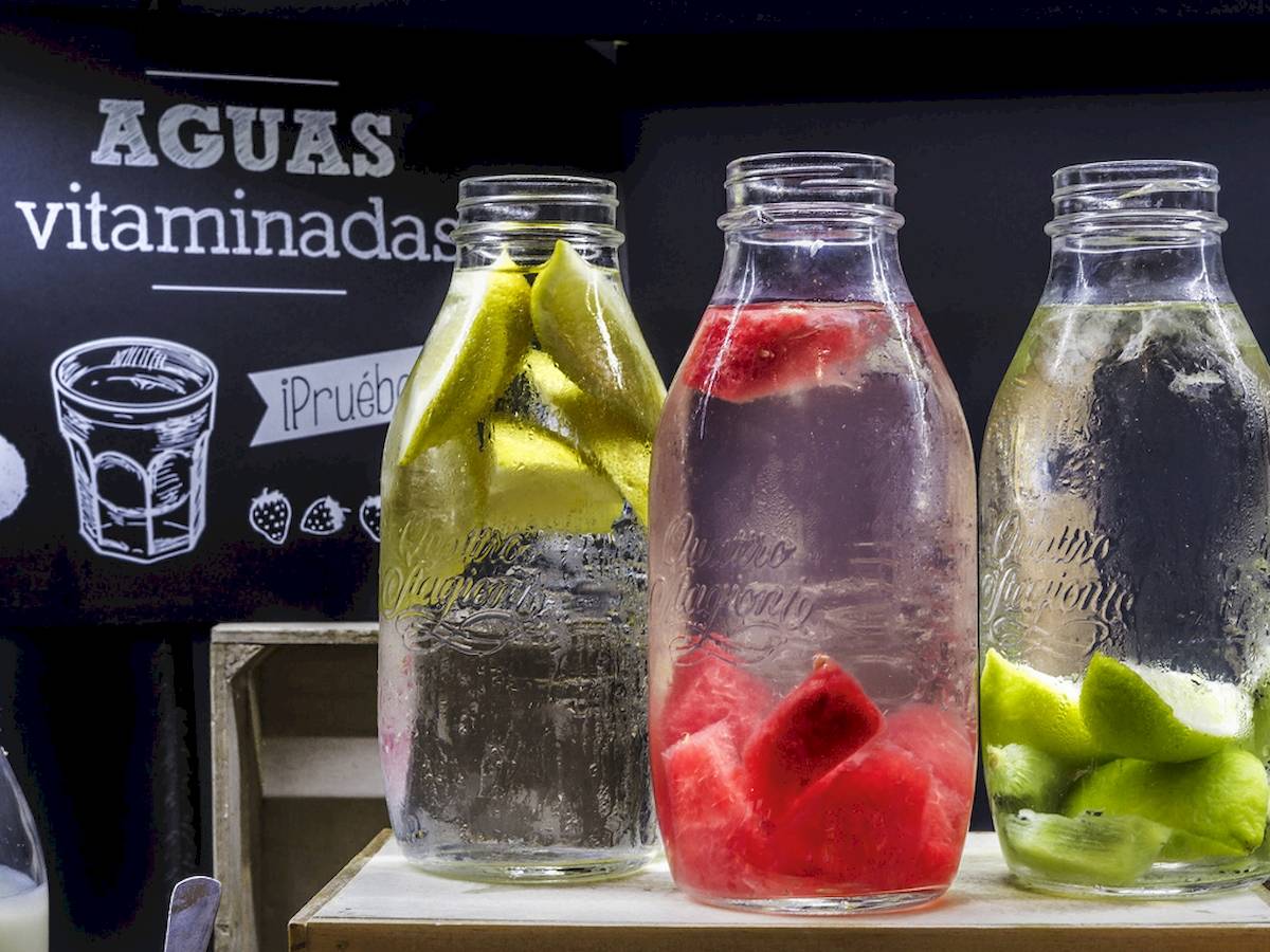 Drei Gläser mit Wasser und Fruchtscheiben, eines mit Gurkenscheiben, eines mit Wassermelonenscheiben und eines mit Limettenscheiben.