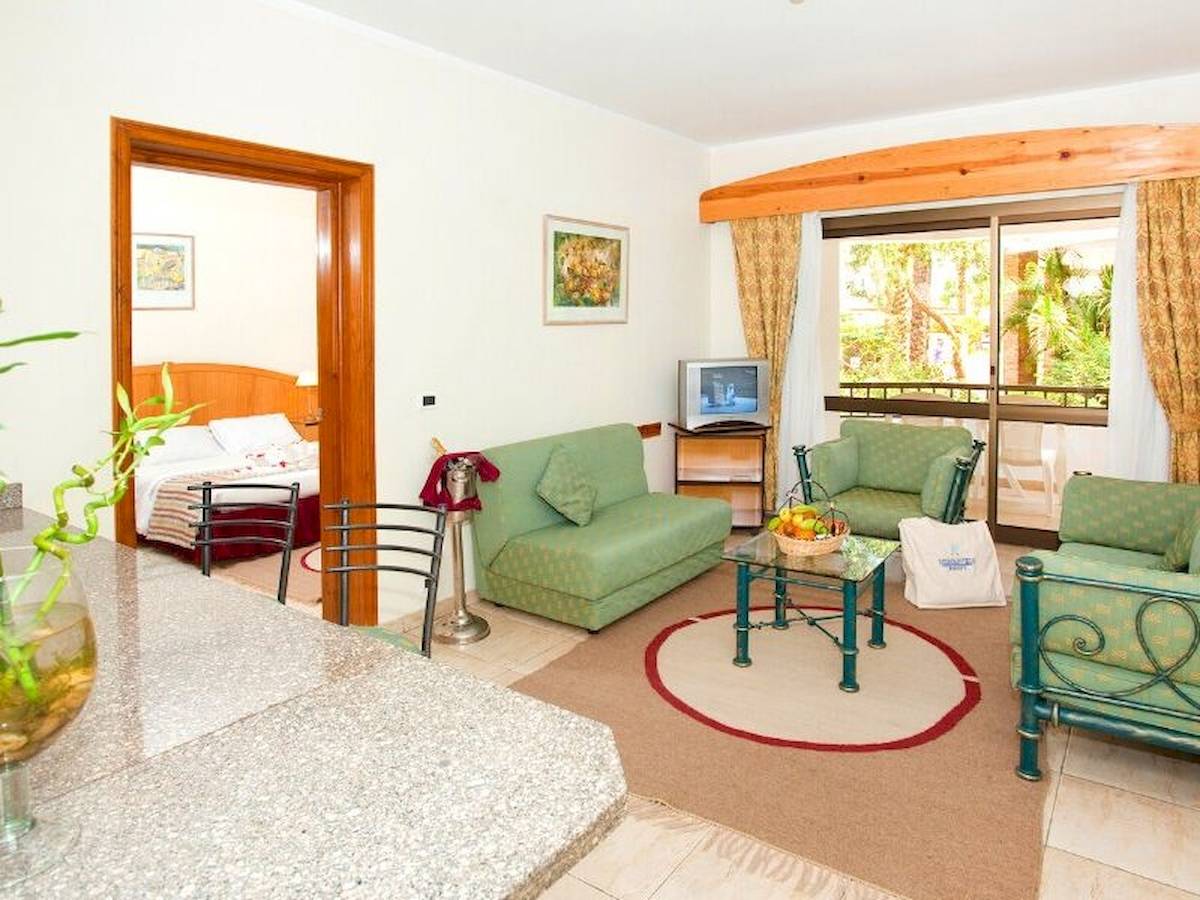 Wohnbereich des Siva Grand Beach Hotels mit grünen Möbeln, Fernseher und Balkonzugang.