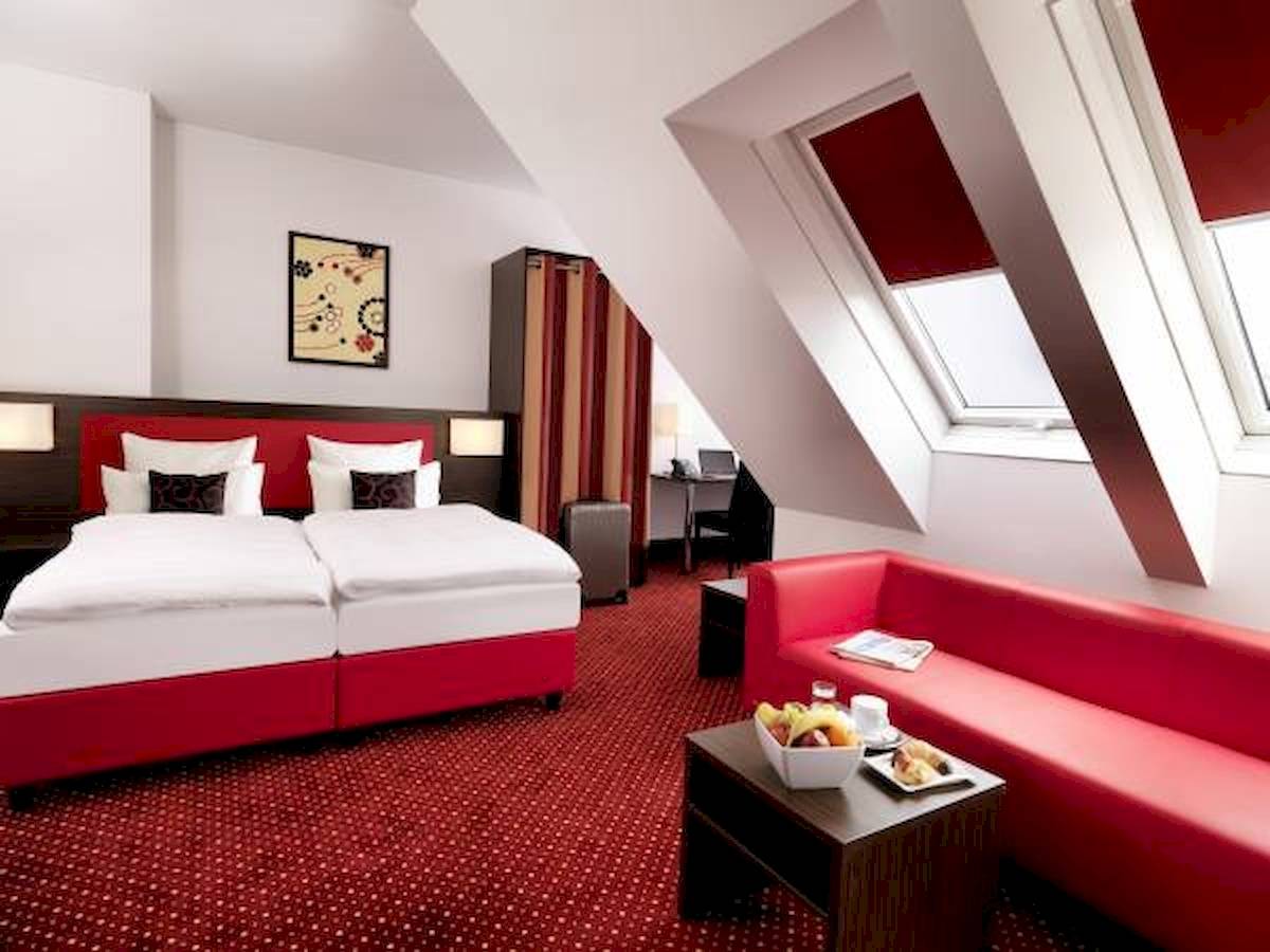 Best Western Plus Amedia Wien Zimmer mit rotem Bett und Sofa.