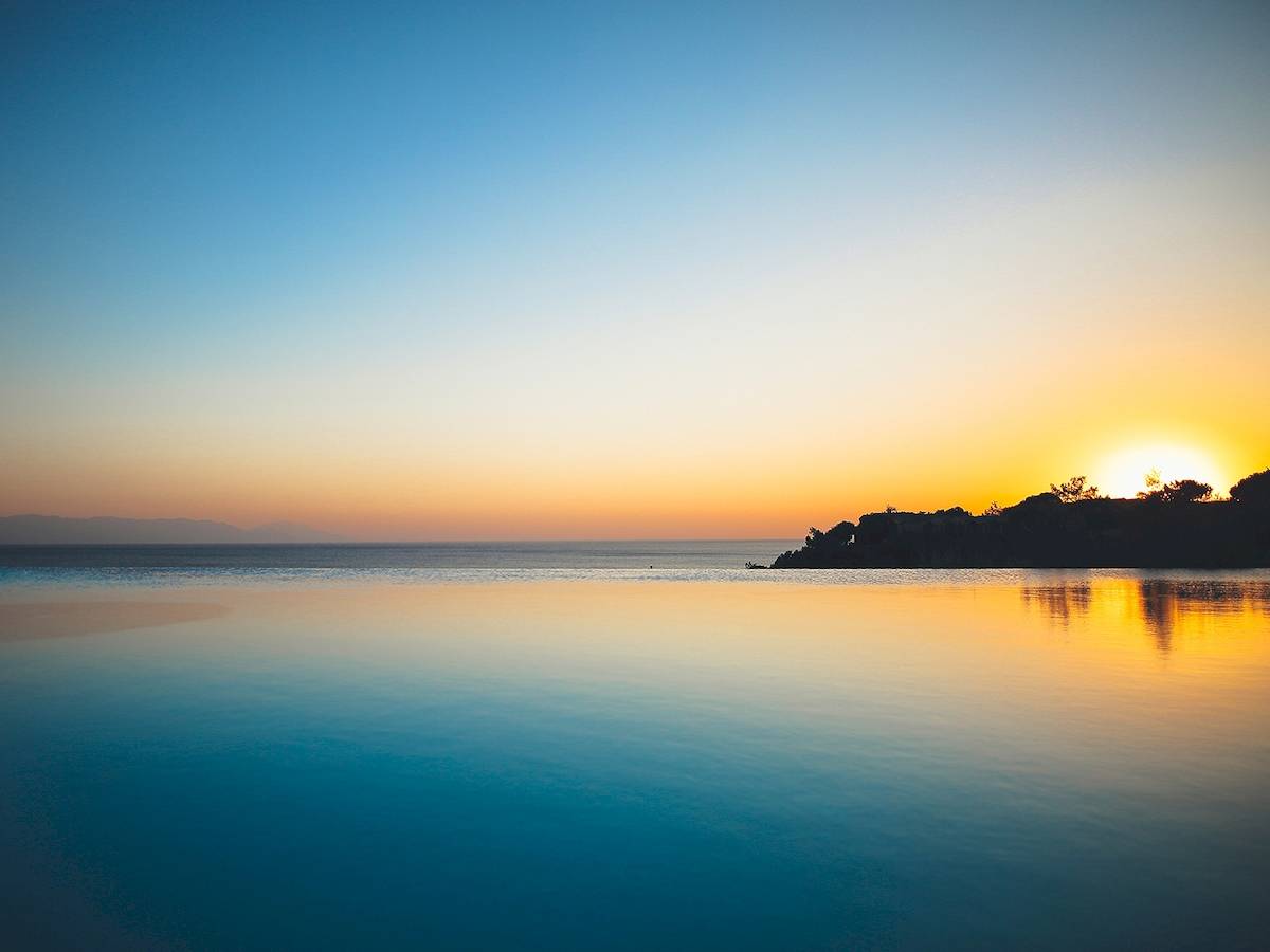 Sonnenuntergang über dem Meer mit einem kleinen Felsen in der Mitte, Club Marvy im Hintergrund