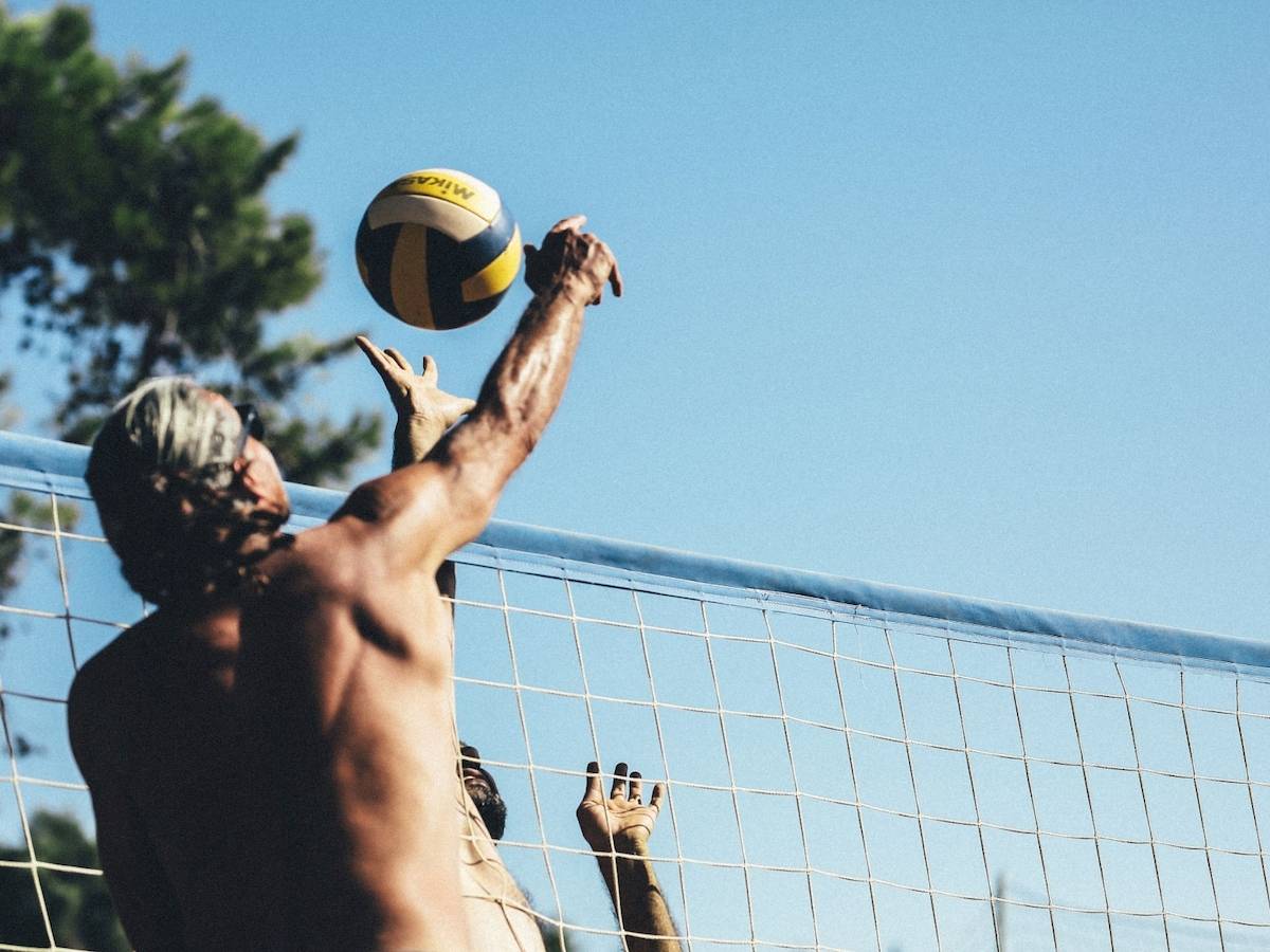 Zwei Männer spielen Volleyball vor einem Netz an einem sonnigen Tag.