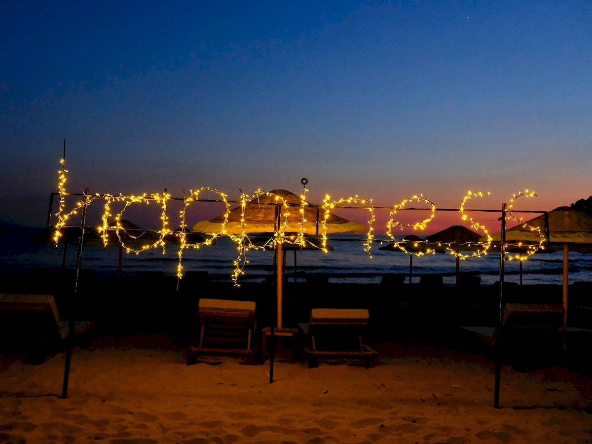 Lichterketten auf einem Strand, die 'Happiness' bilden, mit Club Marvy im Hintergrund.