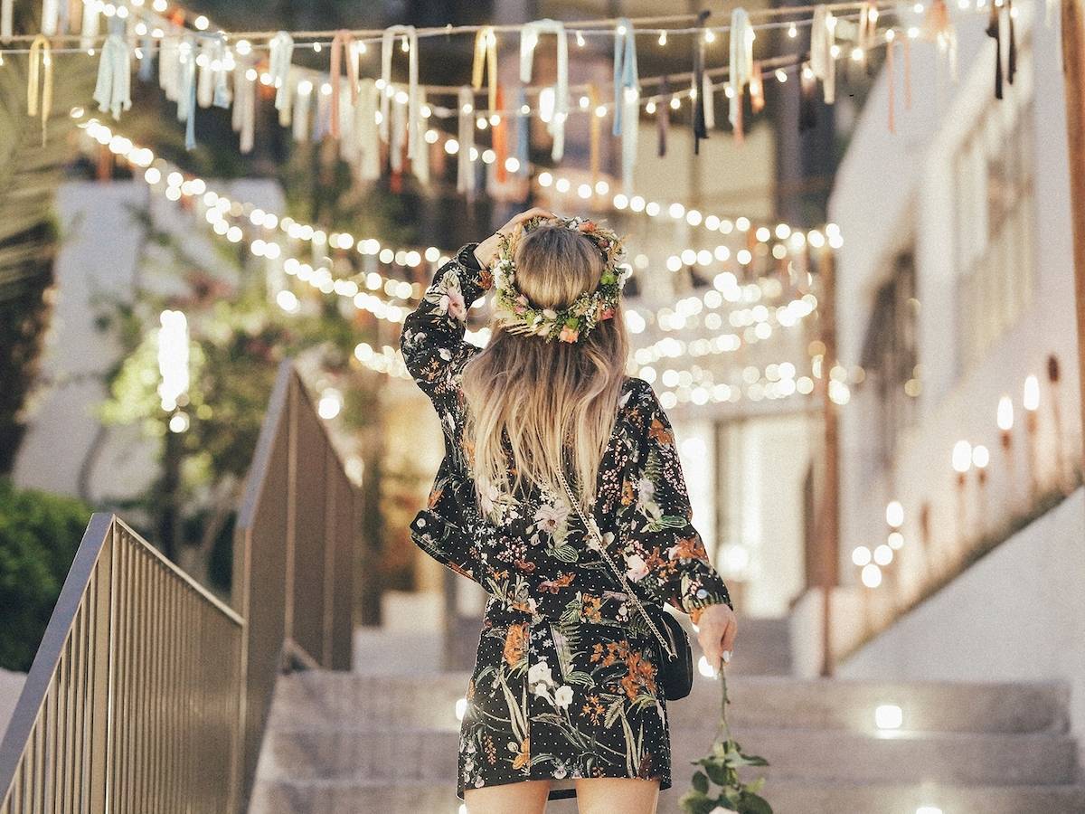 Rückansicht einer Frau mit Blumenkranz, die eine beleuchtete Treppe hinaufgeht.