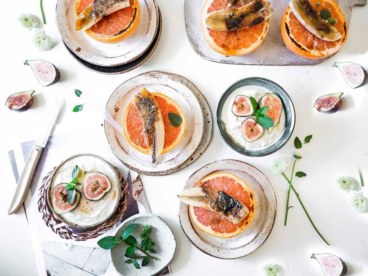 Mehrere Teller mit Fisch in Orangensaft und frischen Feigen auf einem Tisch angerichtet.