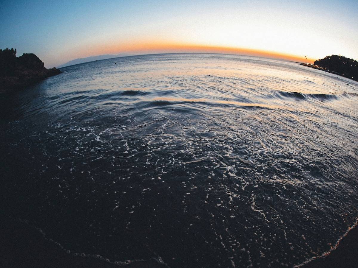 Meer bei Sonnenuntergang mit sanften Wellen und einem Horizont, der von warmen Farben beleuchtet ist.
