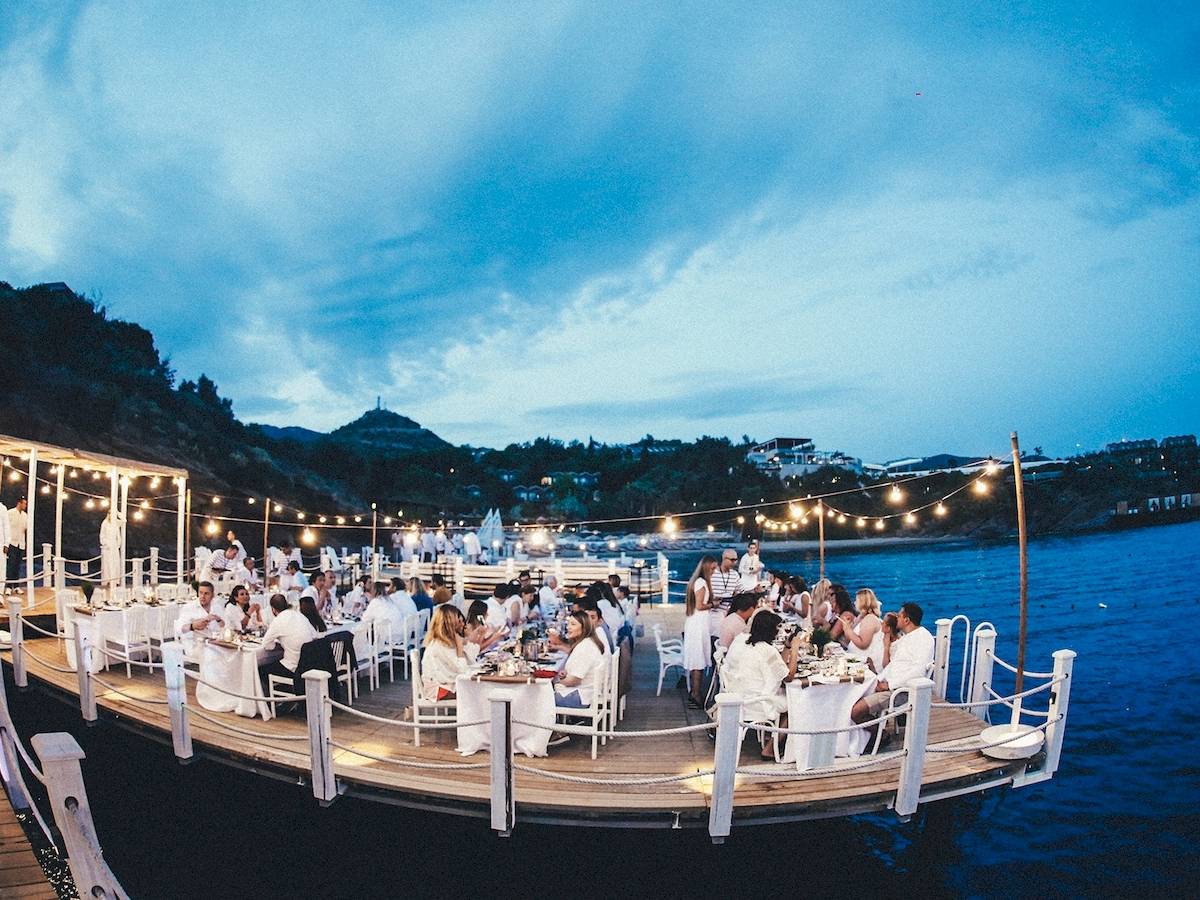 Dinnerparty auf einem Boot mit Gästen, die an langen Tischen sitzen, bei Nacht.