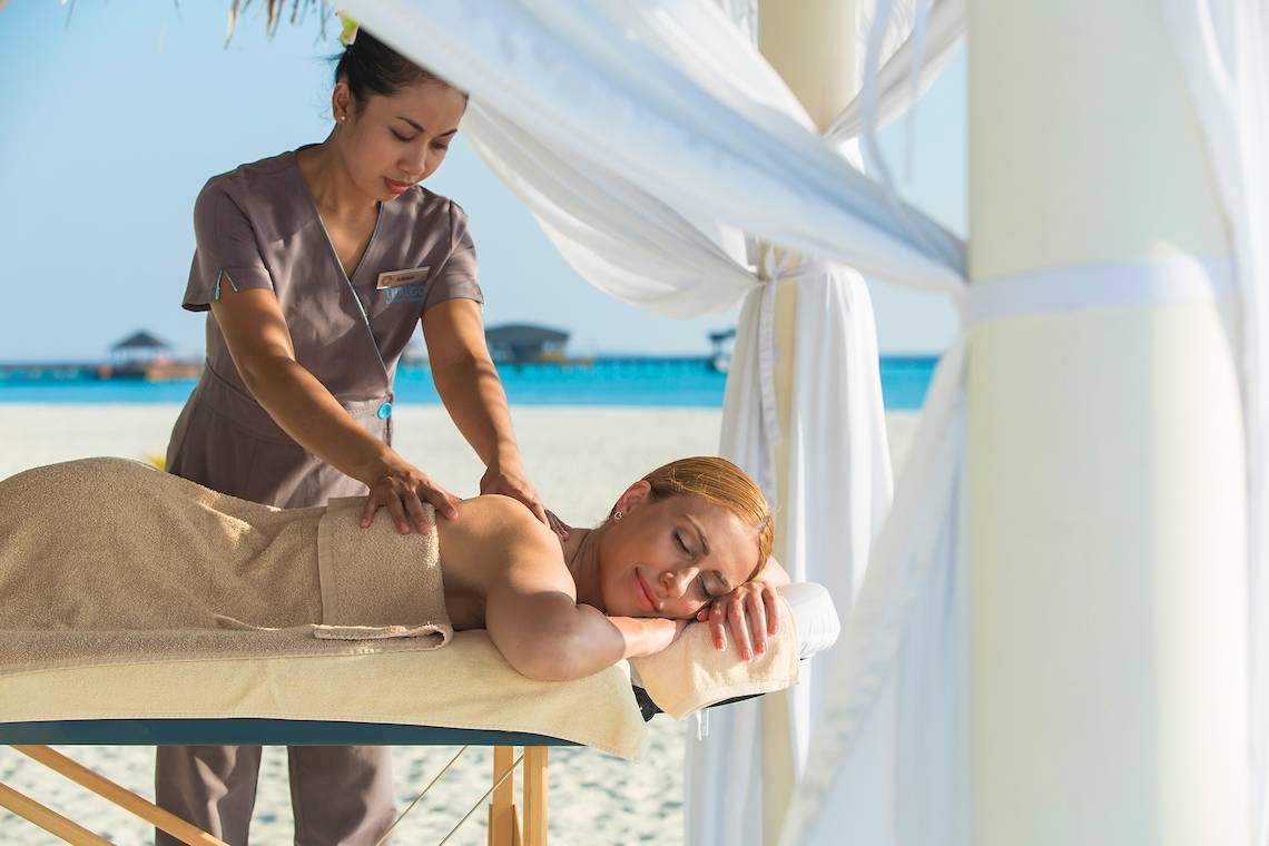 Eine Frau genießt eine Massage am Strand im Sun Siyam Iru Fushi Hotel.