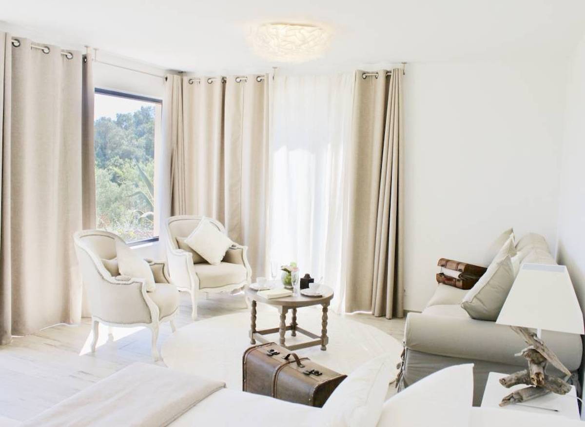 Wohnzimmer von L'Hostellerie du Moulin mit weißen Möbeln, heller Beleuchtung und Blick auf Bäume.