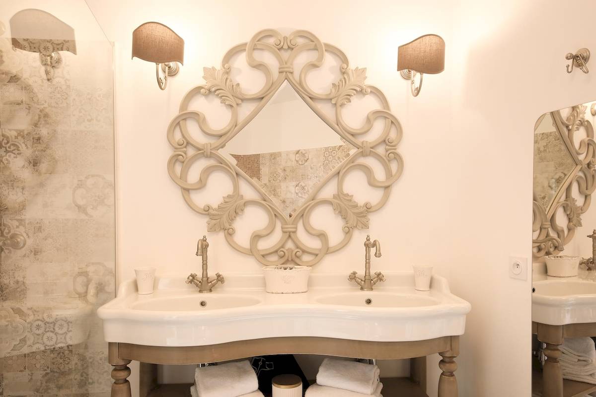 Badezimmer von L'Hostellerie du Moulin mit zwei Waschbecken und einer runden Wandspiegel.