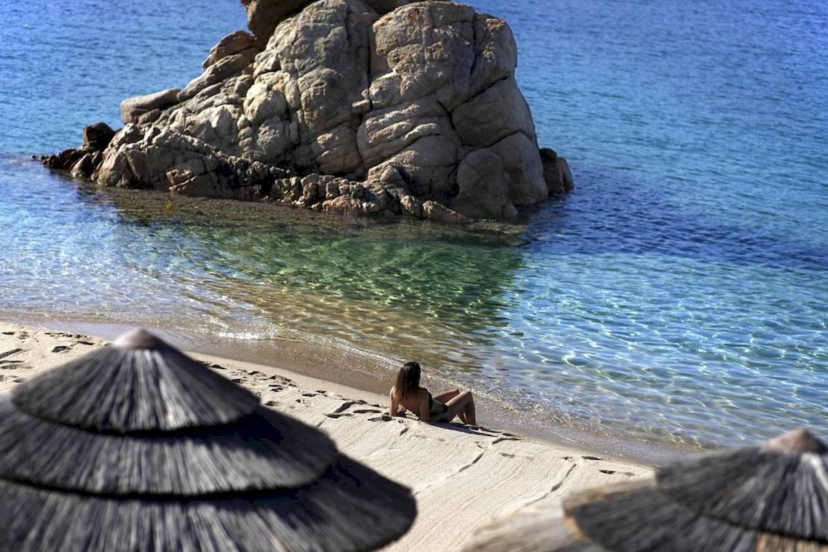 Eine Frau sitzt am Strand vor einem großen Felsen im Wasser.