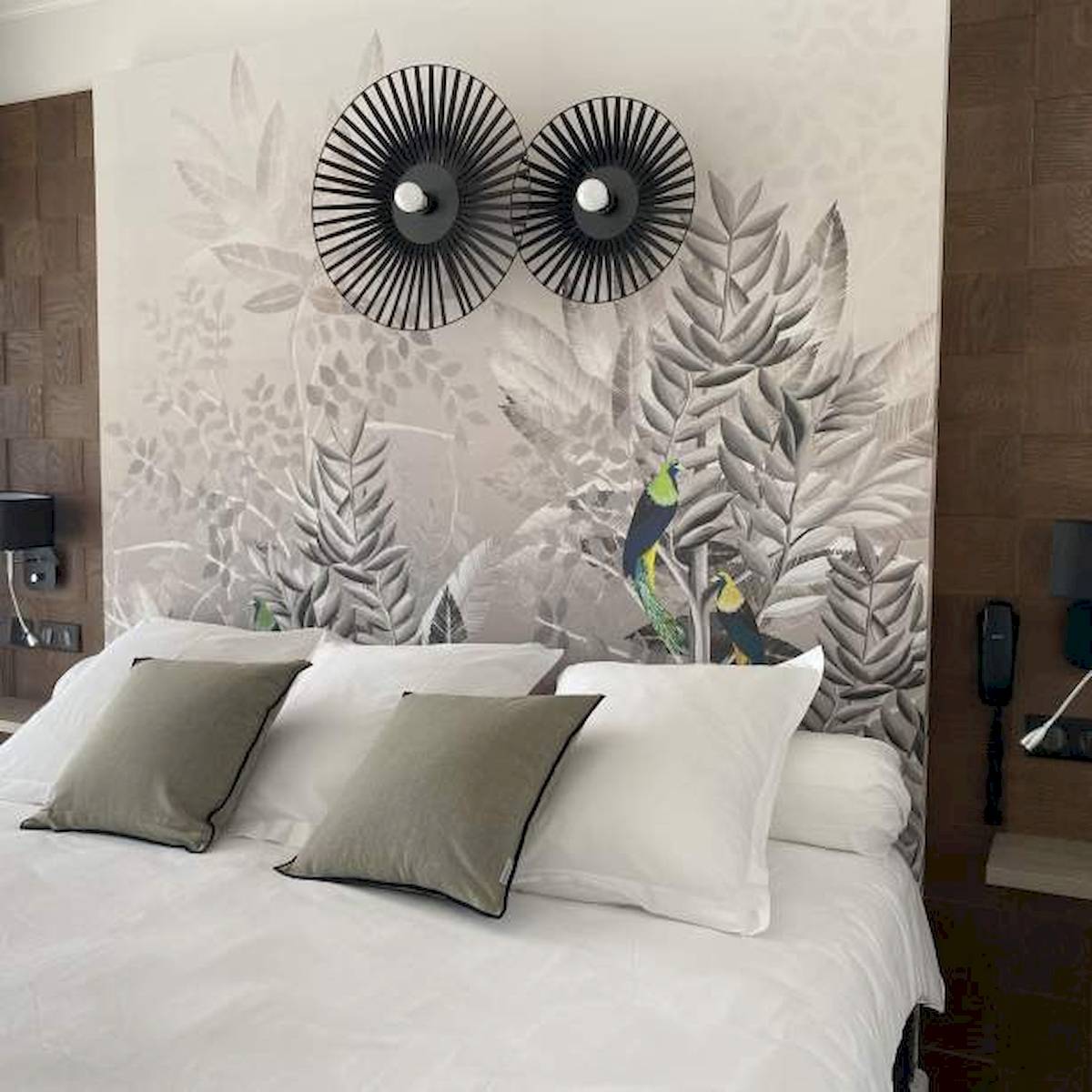 Ein Bett mit weißen Laken und grauen Kissen vor einer Wand mit exotischen Vogelmalereien im La Lagune Hotel.