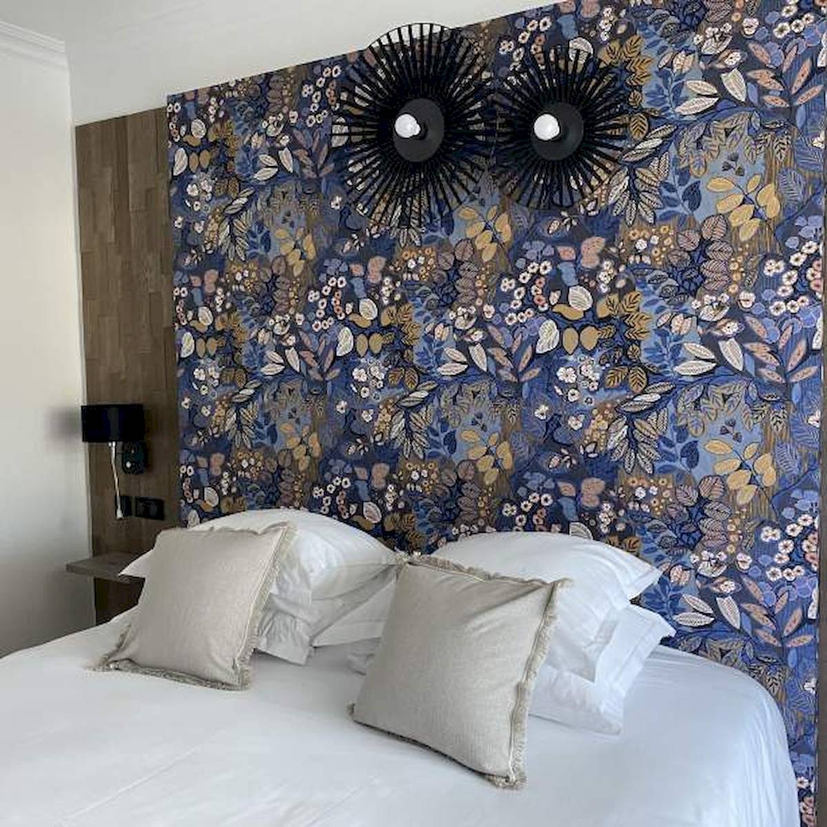 Ein Bett mit weißen Laken und Kissen vor einer blauen Blumentapete im Hotel La Lagune.