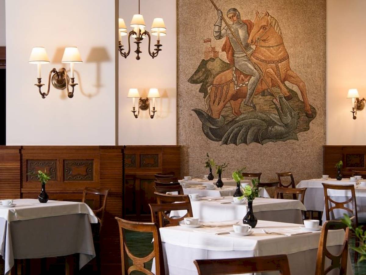 Innenraum des Bettoja Hotel Mediterraneo mit Tisch, Stühlen und Wandbild.