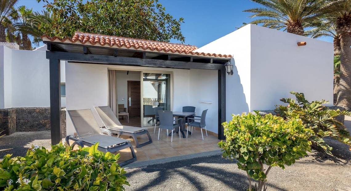 Außenterrasse des Barcelo Fuerteventura Castillo Hotels mit Loungestühlen, Tisch und Palmen im Hintergrund.