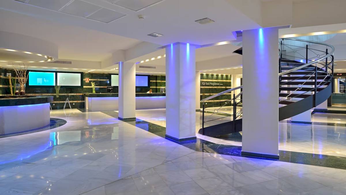 Hotellobby von Sol Milanos Pinguinos mit Empfangstresen, Monitoren und einer Wendeltreppe.