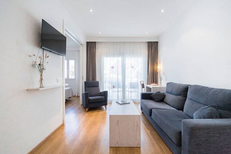 Wohnzimmer des Princesa Playa Hotels mit einem Fernseher an der Wand, einem Sofa, einem Stuhl und einem Tisch.