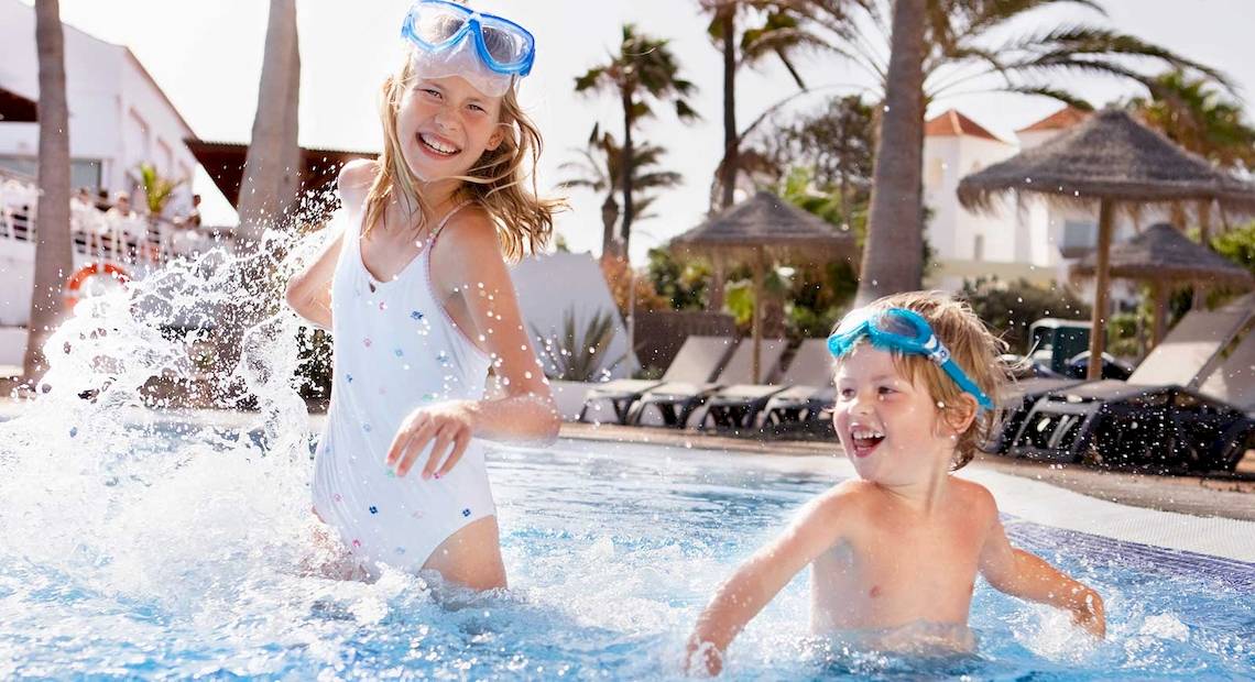 Zwei Kinder schwimmen und lachen im Pool des Barcelo Fuerteventura Castillo Hotels.