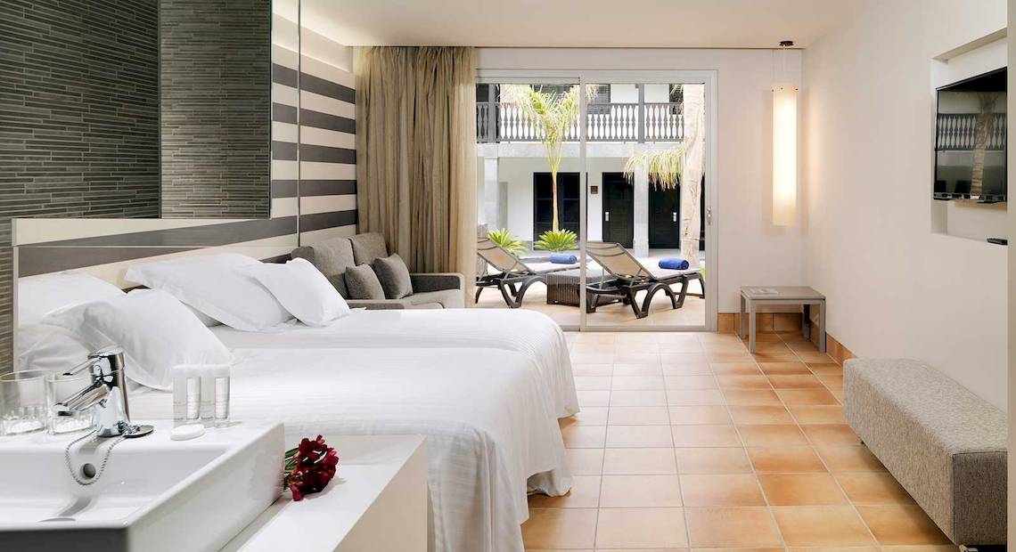 Hotelzimmer im Barcelo Fuerteventura Castillo mit zwei Betten, Wohnzimmerbereich und Terrasse.