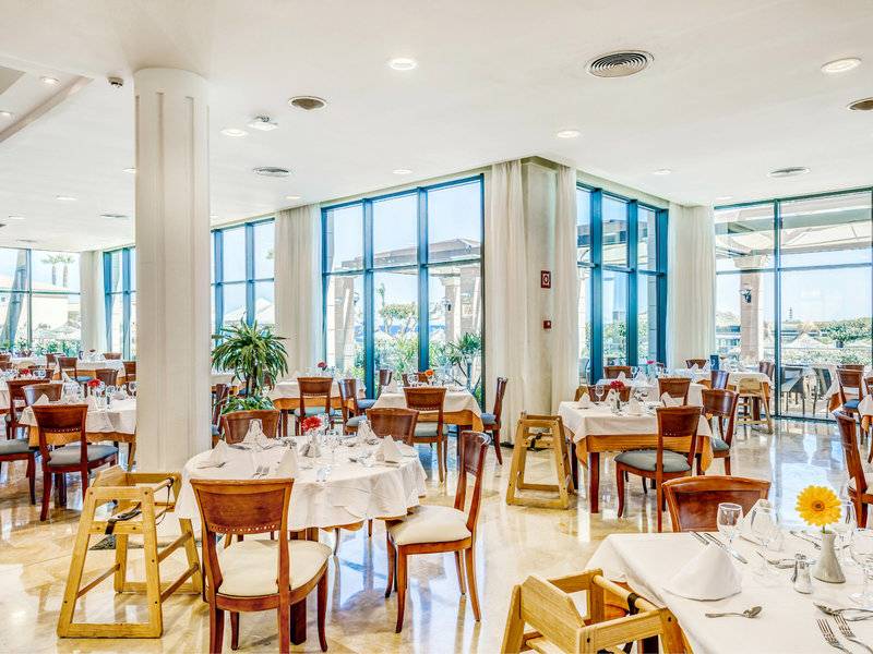 Innenansicht des Restaurants im Punta Prima Resort & Spa mit gedeckten Tischen und großen Fenstern.