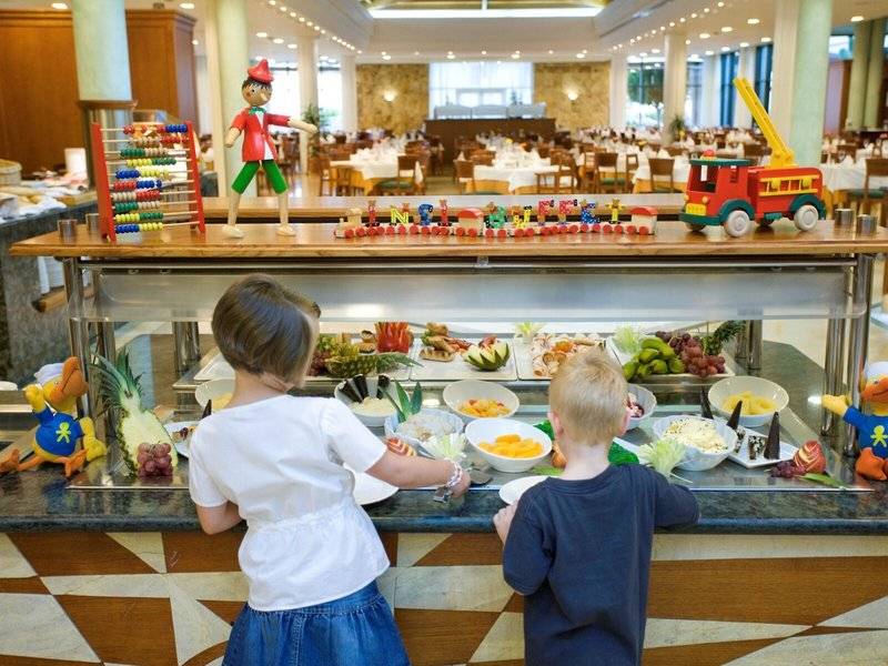 Zwei Kinder stehen vor einem Buffet im Punta Prima Resort & Spa mit verschiedenen Früchten und Dekorationen.