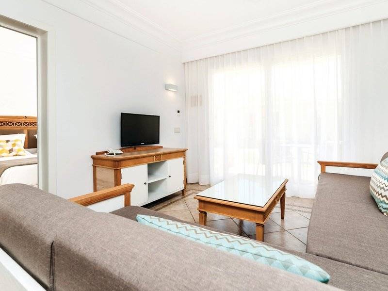 Innenansicht des Wohnzimmers im Punta Prima Resort & Spa mit Fernseher, Couch, Tisch und Bett