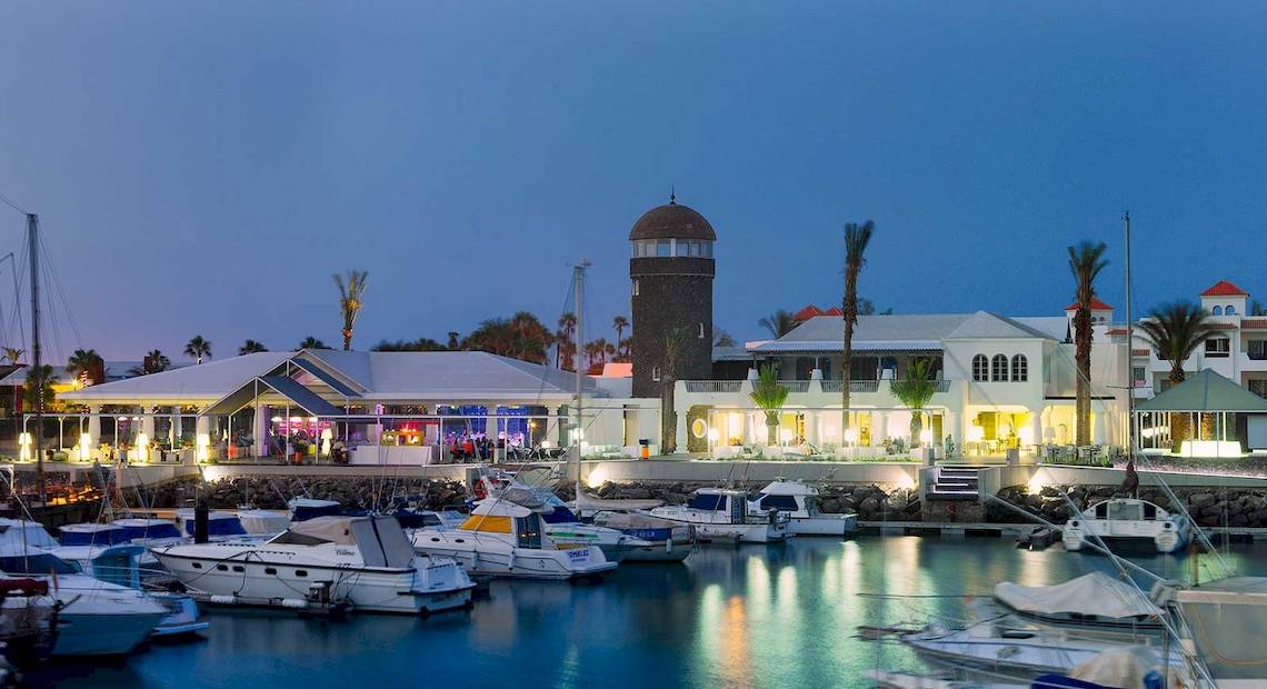 Hafen mit vielen geparkten Booten und dem Barcelo Fuerteventura Castillo Hotel im Hintergrund.